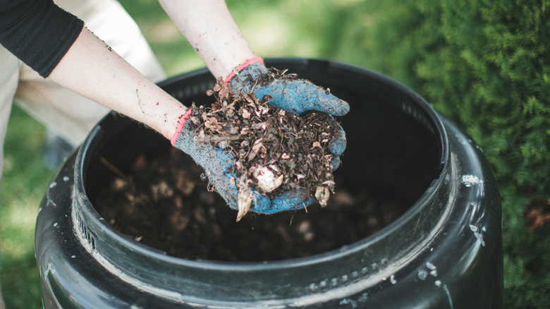Gloved hands holding a pile of compost over a black barrel