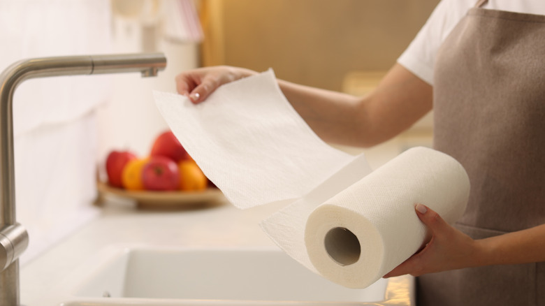 Sheets are being torn from a paper towel roll by someone standing in front of a kitchen sink
