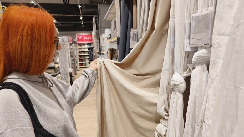 woman looking at beige curtains in store