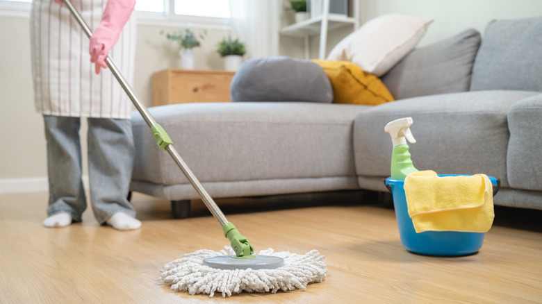 Someone cleaning laminate floor with microfiber mop, with bucket, spray bottle, and microfiber cloth