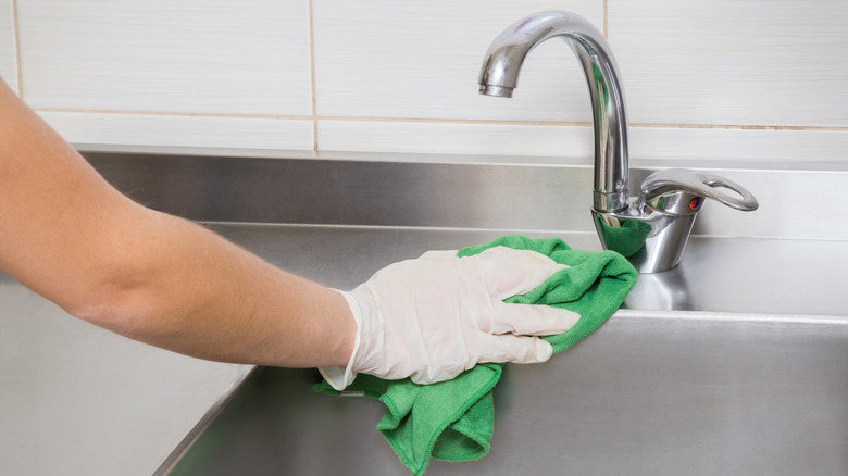 gloved hand cleaning stainless steel sink with microfiber cloth