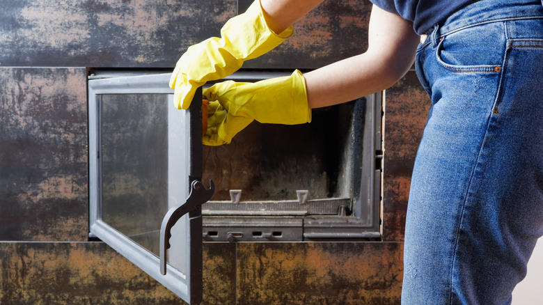 A person examines the glass door of a fireplace while wearing gloves