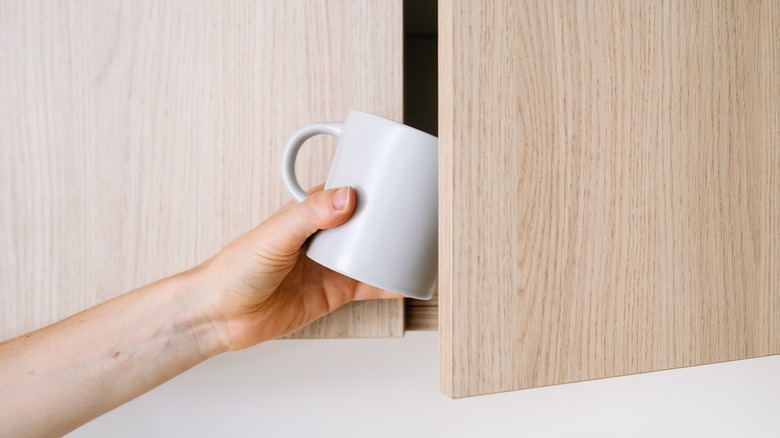 Person putting a mug in cabinet