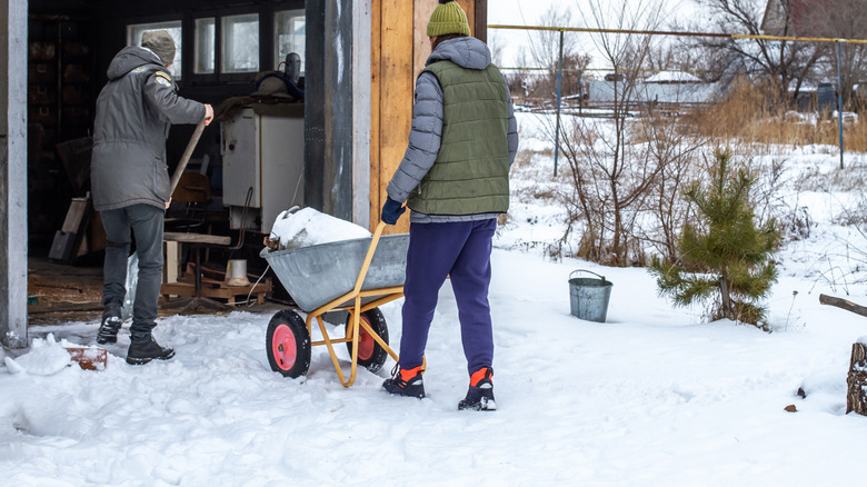Two men working in the snow in front of a garage with the door open.