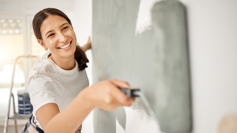 A woman smiling while painting a room gray