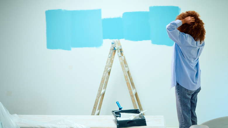 A stressed woman looking at blue paint swatches on a wall