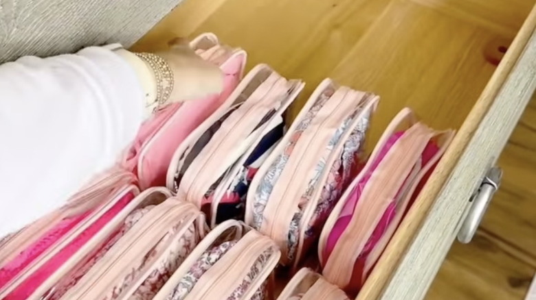 A person places clear bags of clothing in a dresser drawer