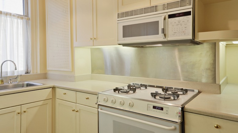 A small kitchen with light yellow cabinets, white stove, and white microwave