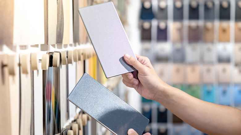 Designer hands compare two gray laminate sheets nearby material swatch wall display in material library.