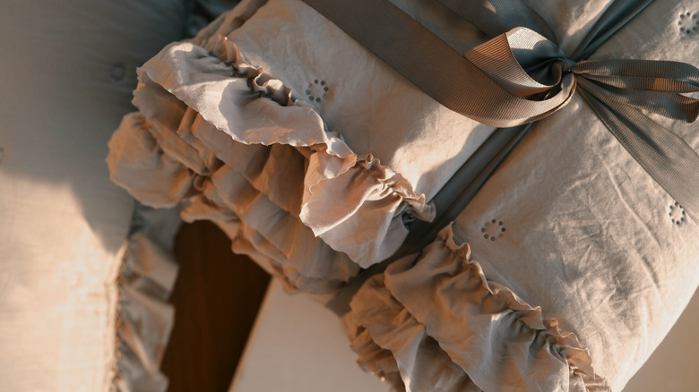 Soft beige bedding set with ruffled details tied with a gray ribbon on a matching beige background.
