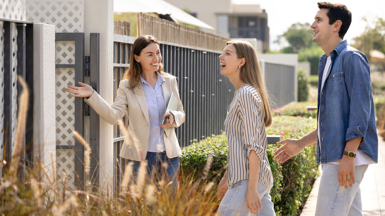 A realtor inviting a couple into viewing a home for sale