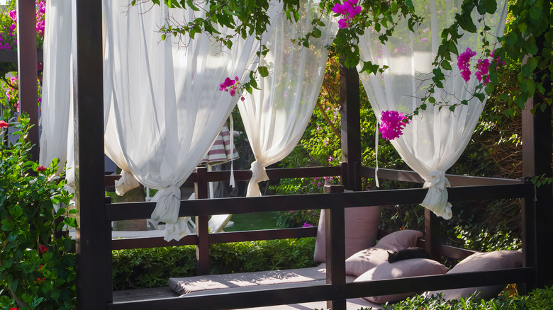 An outdoor sleeping porch with a mattress and white curtains.