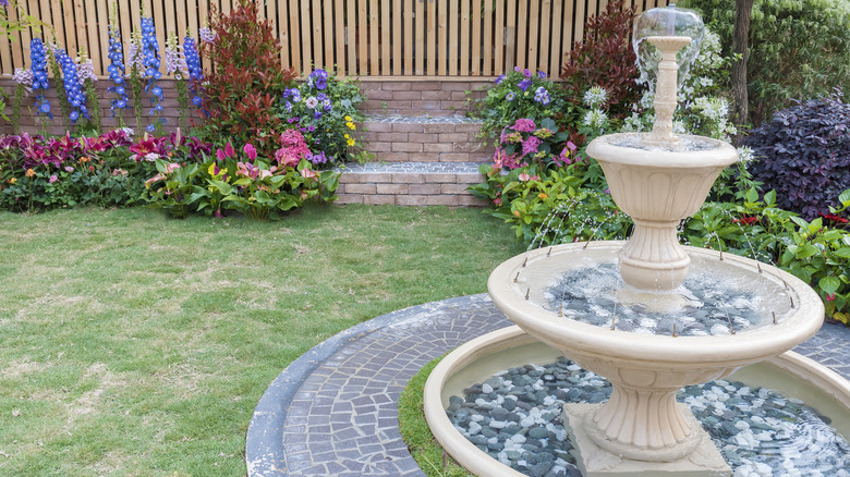A tiered fountain flows in a backyard among colorful flowers.