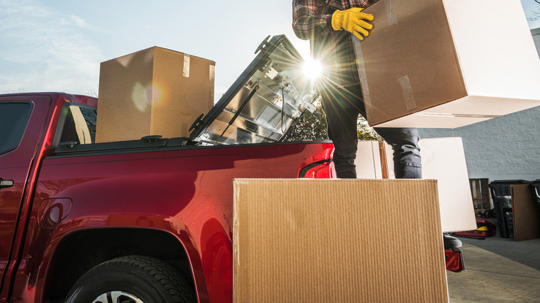 large boxes being put in the back of a red pickup truck by a man with yellow gloves and plaid shirt