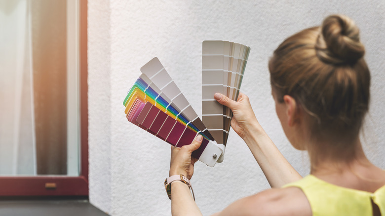 A woman standing in front of a house exterior, looking at paint samples.