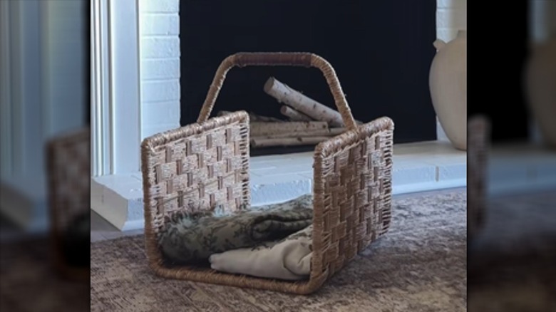 Two blankets are stored in a woven log carrier next to a fireplace.