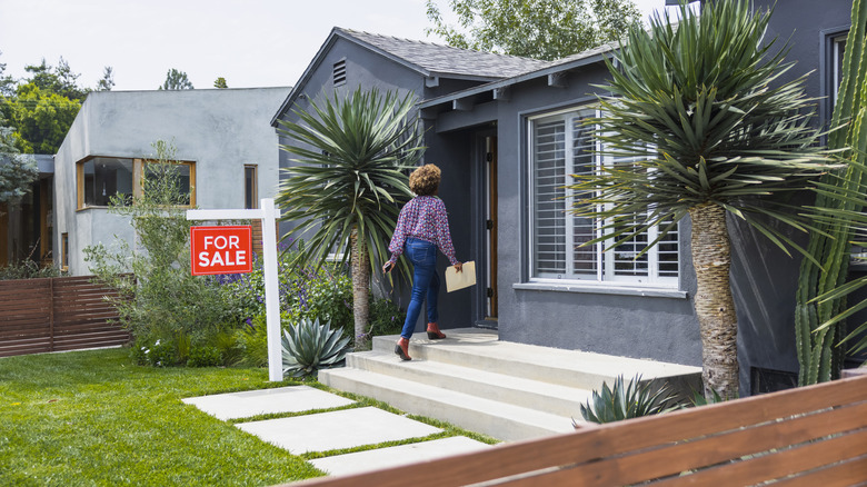 Woman walking up to a home with a for sale sign