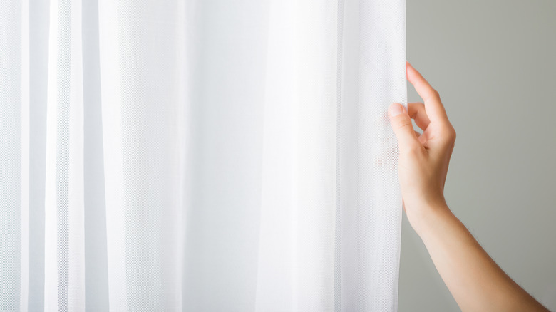 Hand touching white curtains