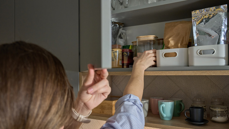 Person reaching into kitchen cabinet