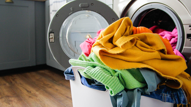 Pile of bright cloths in laundry basket placed in front of an open washing machine