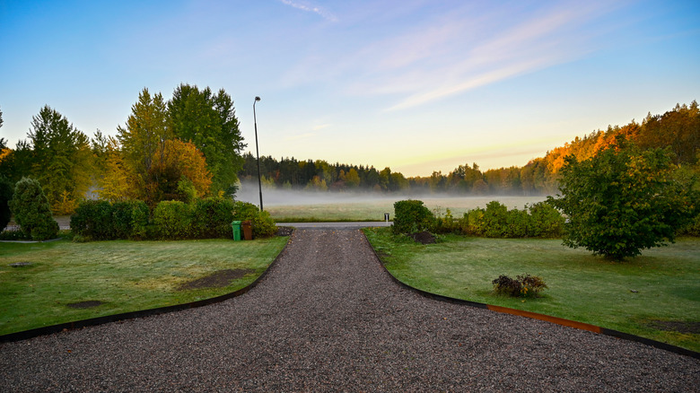 Wide view of a gravel driveway in front of a foggy meadow of grass
