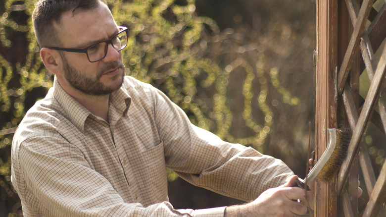 A man cleans a trellis with a wire brush.