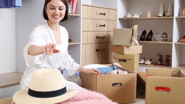 A woman reaches for a hat while she is organizing her walk-in closet.
