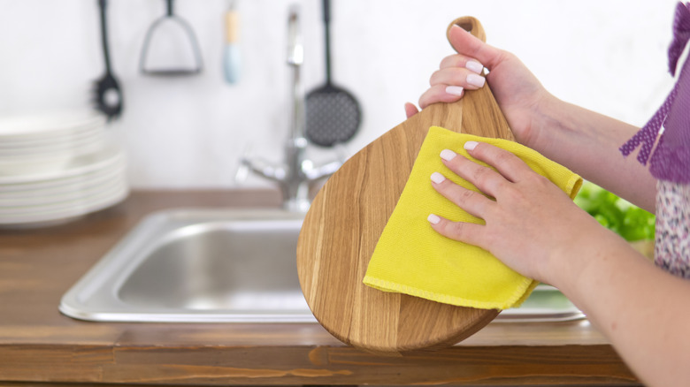 Woman wiping down wood cutting board with clean dish towel.