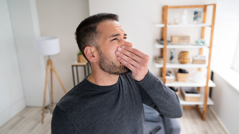 man covering nose in smelling living room