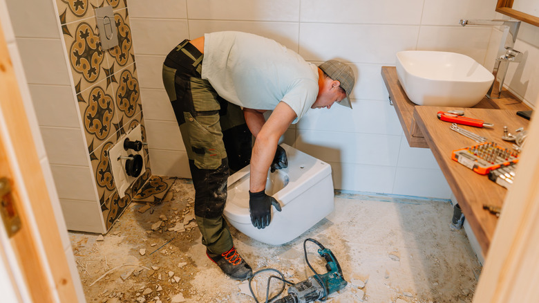 Man moving a toilet bowl while renovating a bathroom