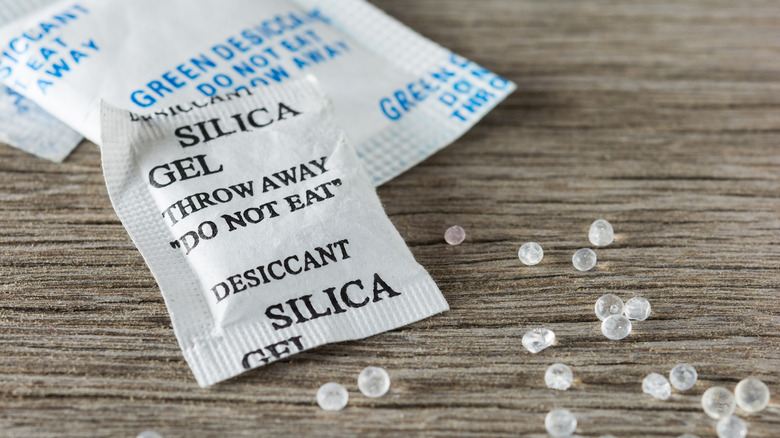 A silica gel packet with clear beads next to it on a wooden surface