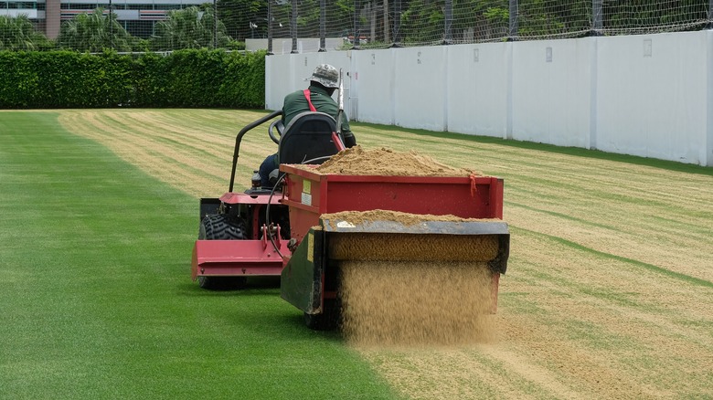 A man on a machine topdressing a lawned area.
