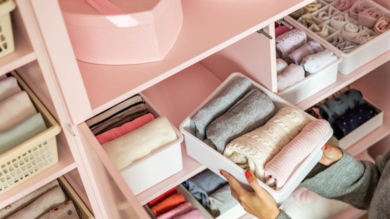 Close up of someone putting a bin of sweaters into a closet organizer