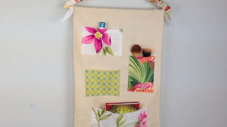 A hanging wall organizer made of a sheet of canvas with handkerchief pockets
