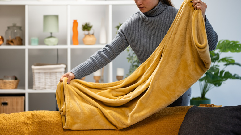 A woman folds a mustard blanket in a living room.