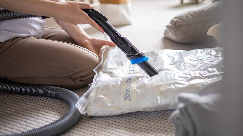A person uses a vacuum to seal a compression bag with a comforter inside it.