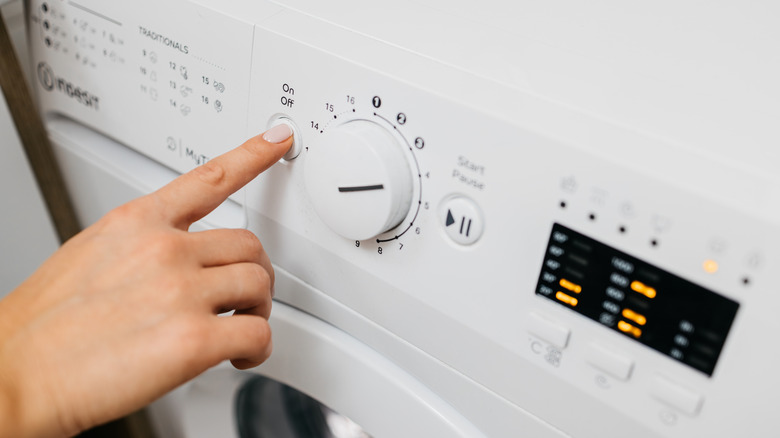 Close up of person pressing power button on washing machine
