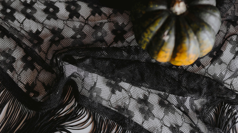 A green and orange pumpkins sitting atop a piece of black lace.