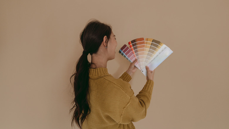 A smiling woman compares a fan of paint display chips to an already painted wall.