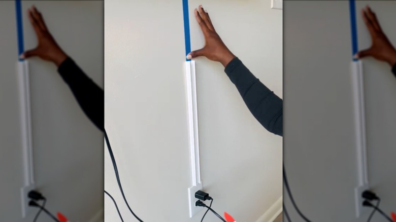 person adding cable hiders to a wall underneath a wall-mounted TV