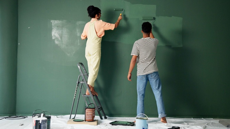 Two people paint interior home walls green
