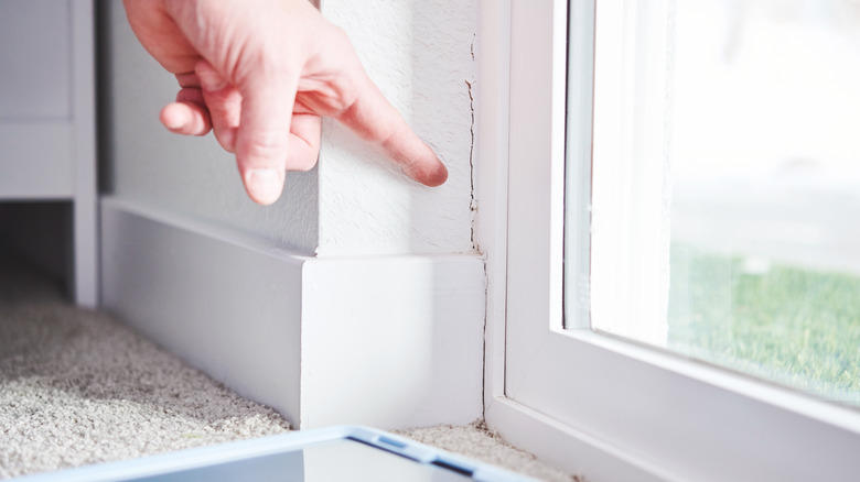 Hand pointing at wall crack in the bottom corner of structure