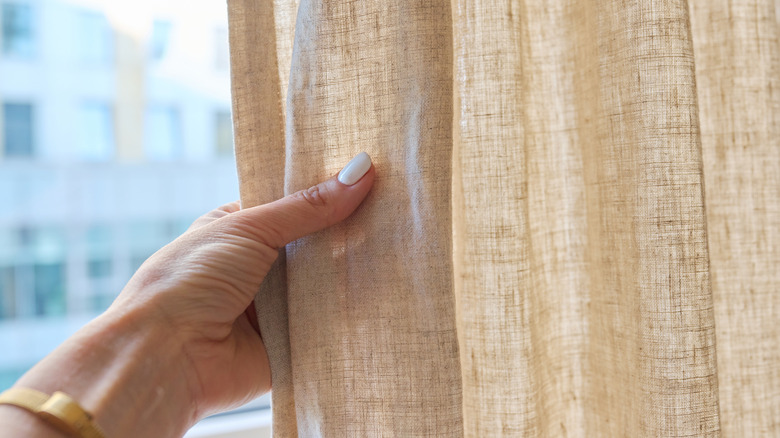 Woman touches a light brown curtain