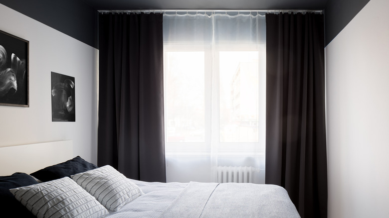A room with a black ceiling, white walls, and black curtains