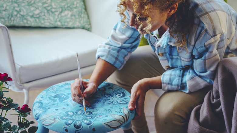 Woman hand painting design on a stool seat.