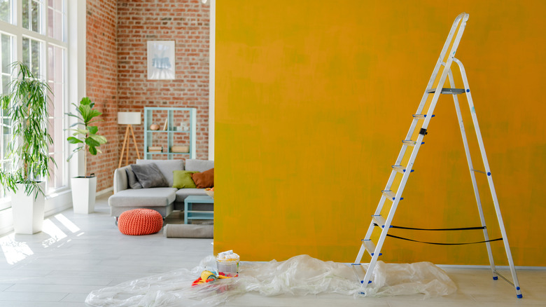 A tall ladder set up in front of a wall with painting supplies on the floor.