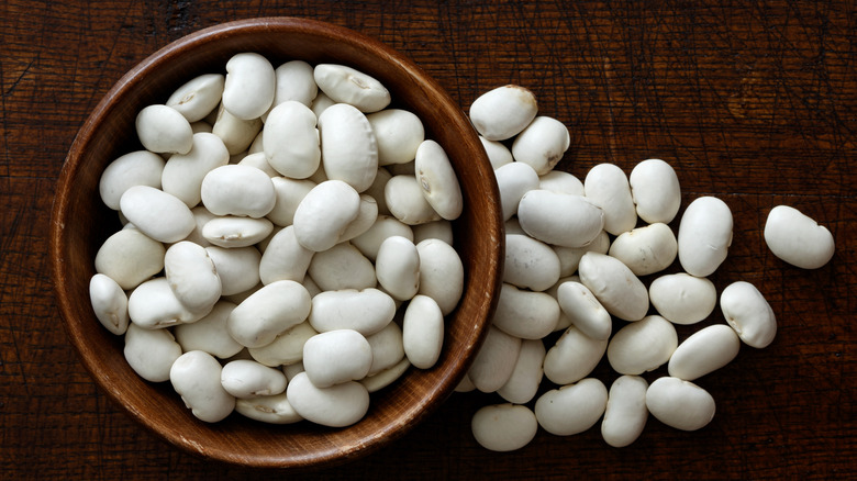 Dry lima beans in bowl and on wood surface