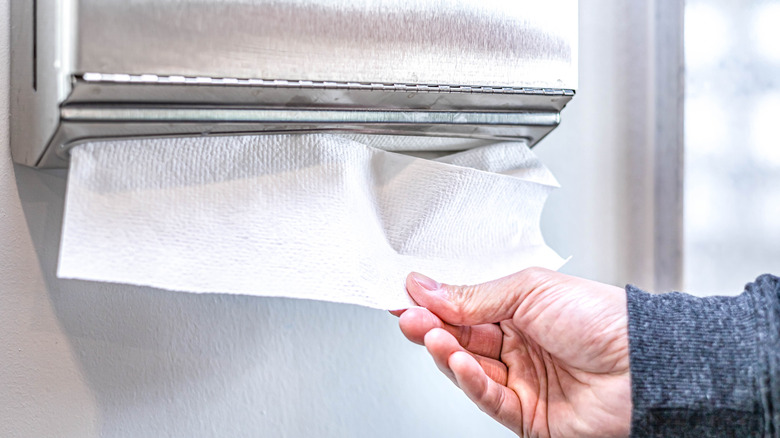 Someone pulling paper towel from dispenser mounted in a bathroom