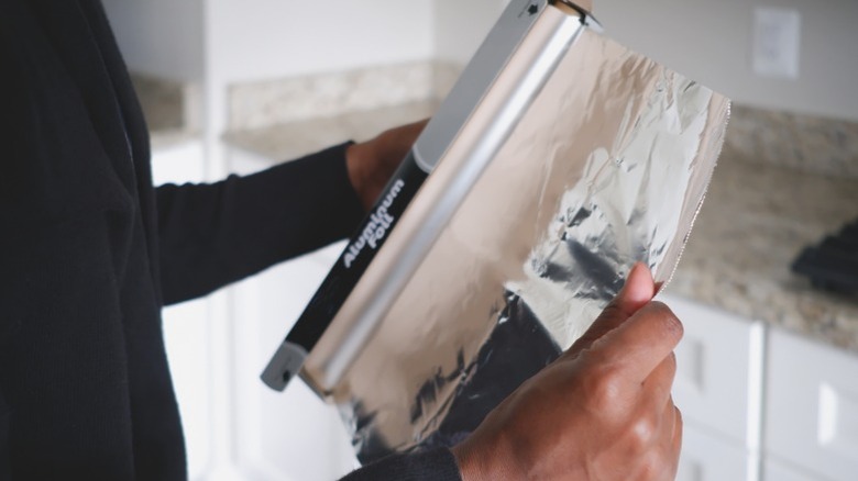 Person in black sweater pulling aluminum foil from roll in kitchen