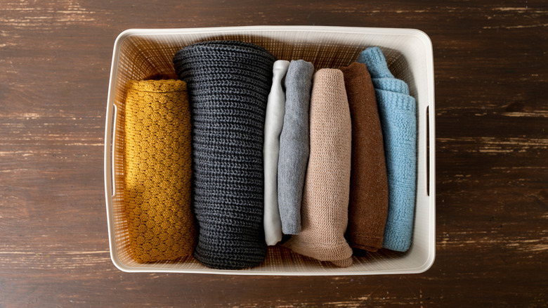 Sweaters folded in a white plastic storage bin with the lid removed.